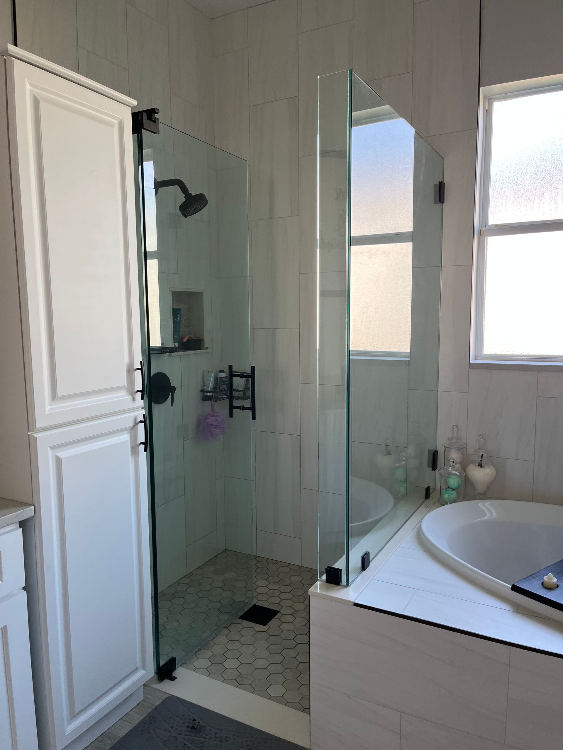 Bathroom with a glass shower, white cabinets, and a bathtub.