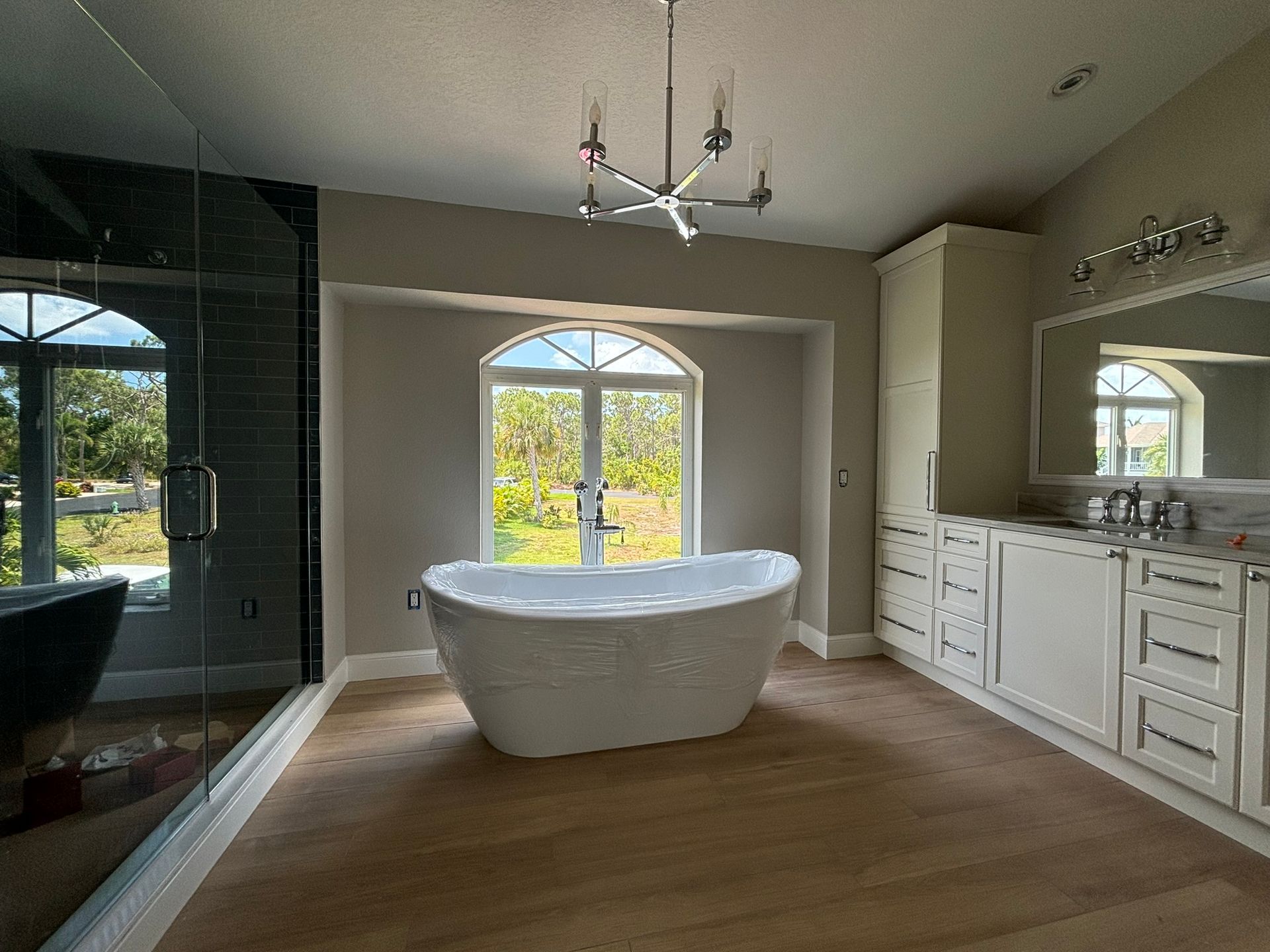 Spacious bathroom with a white freestanding tub by a window, light-colored wood floor, and vanity with a mirror.