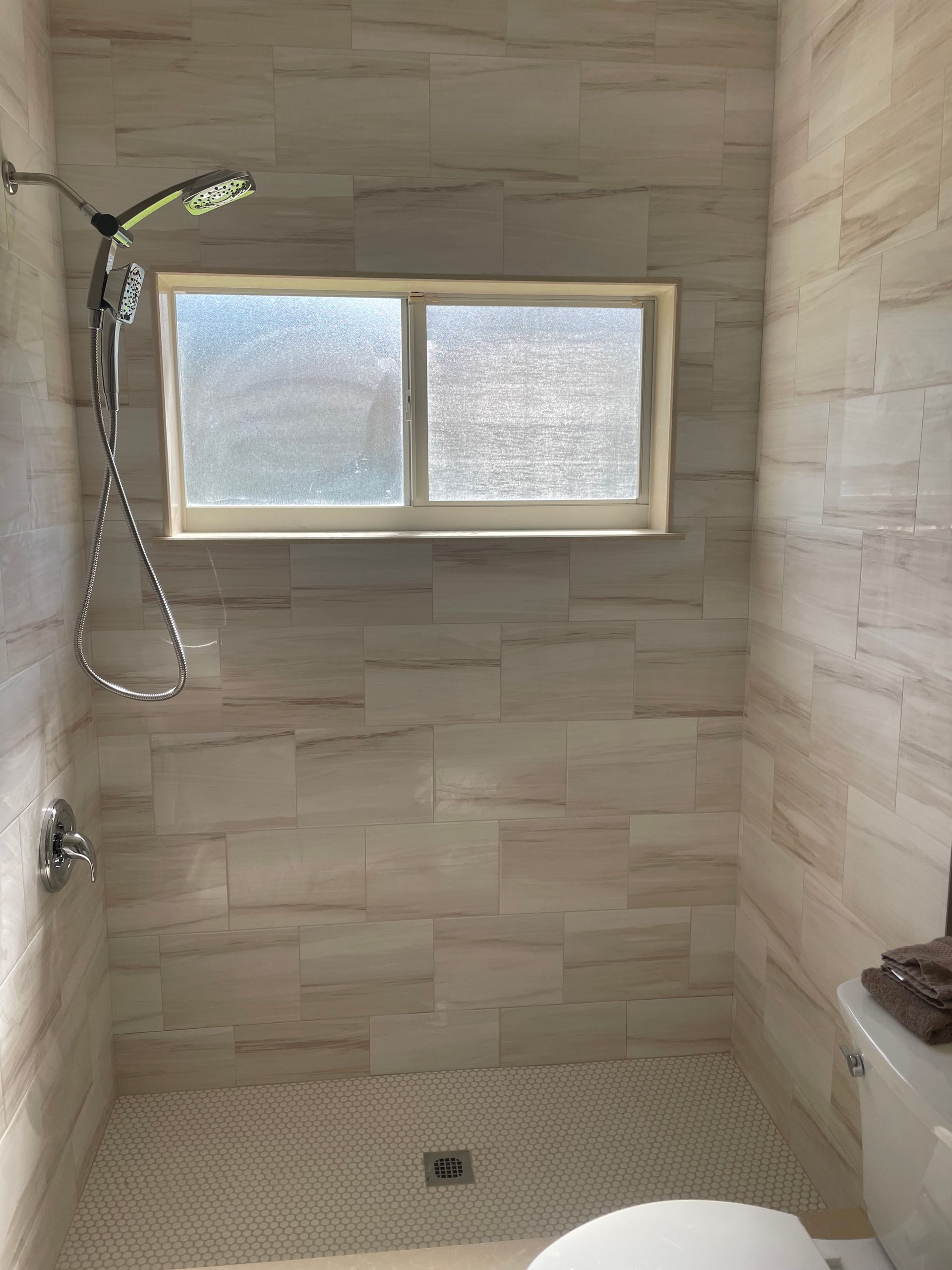 Shower stall with tiled walls and floor, window, and showerhead.
