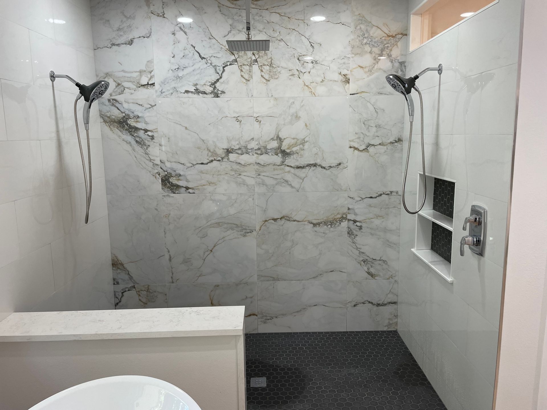 Modern shower with marble-look tile, two showerheads, and dark pebble floor.