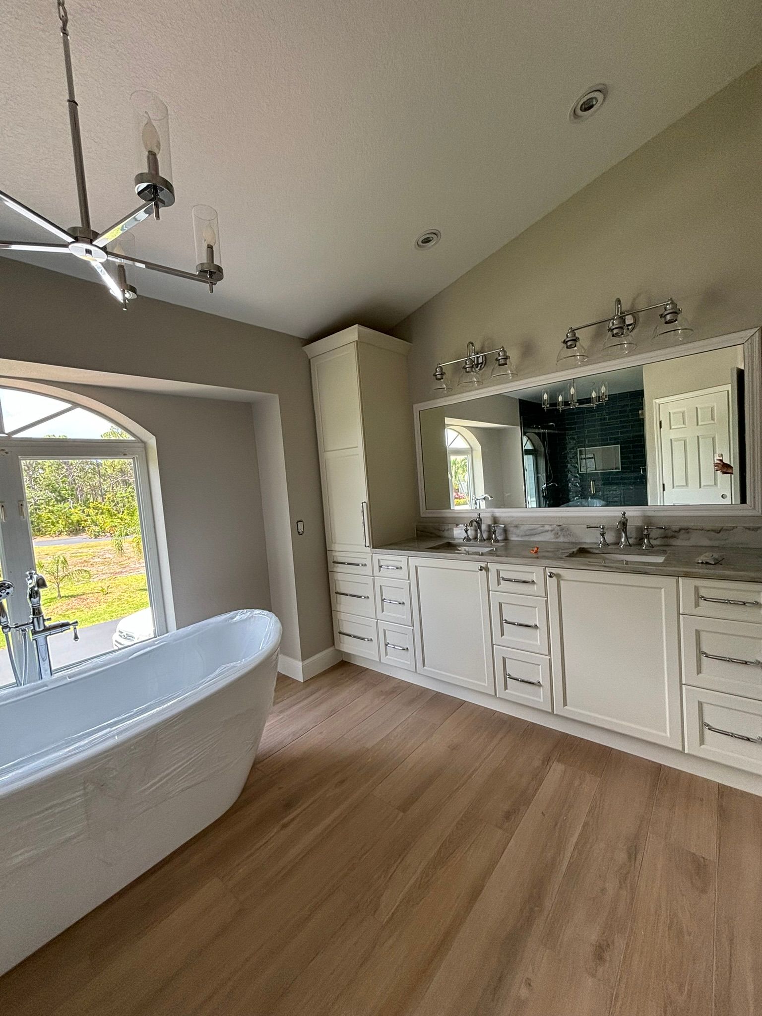 Modern bathroom with a white tub, white cabinets, a large mirror, and wood flooring.