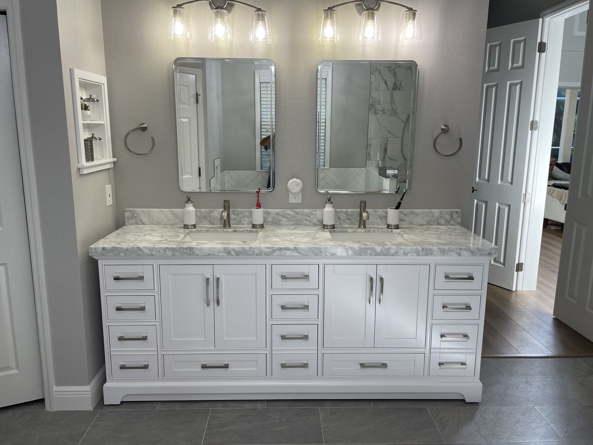 White double vanity with mirrors, lights, and marble countertop in a bathroom.