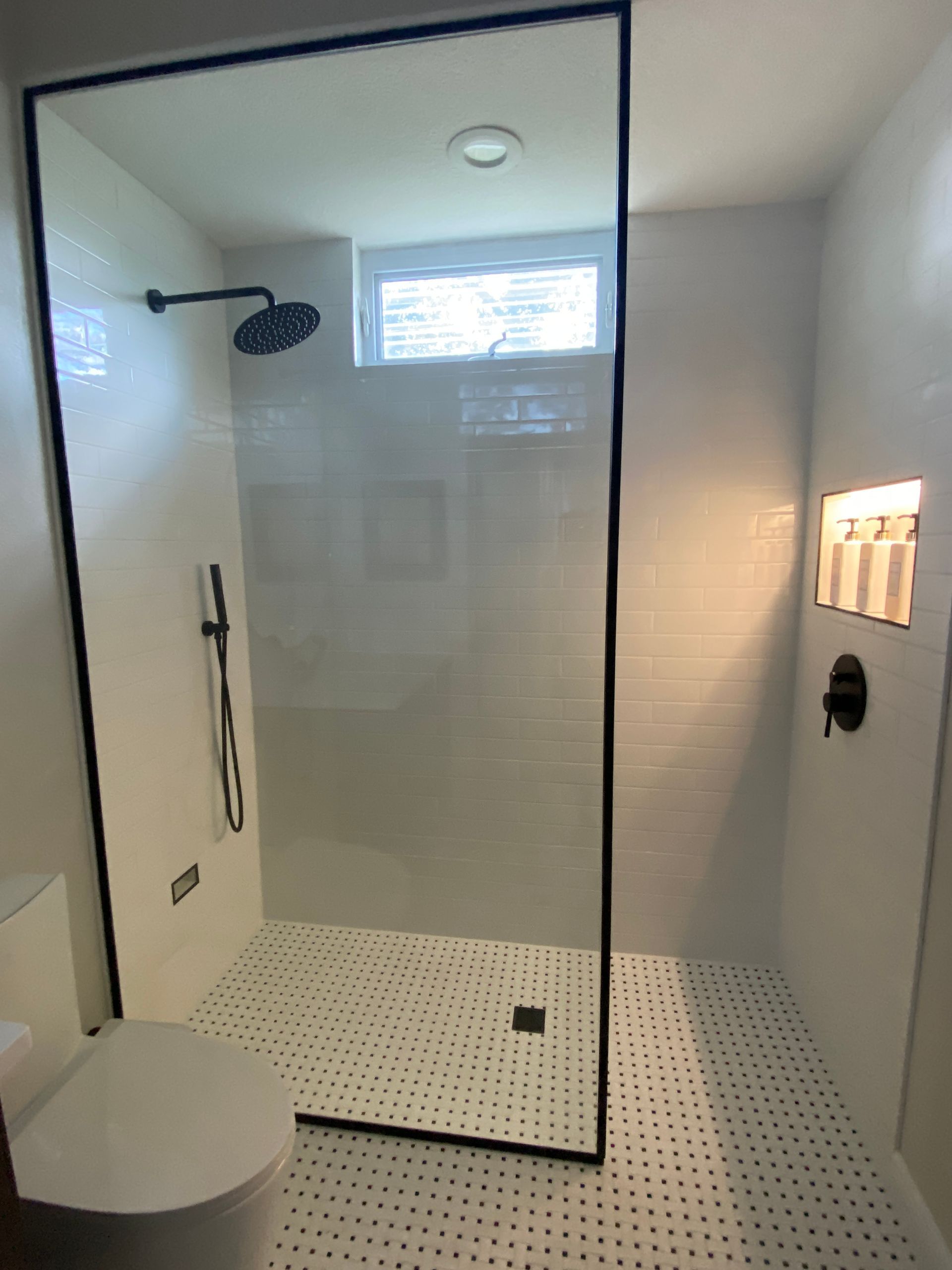 Modern bathroom with a glass-enclosed shower, black fixtures, white tiled walls and floor, and a toilet.