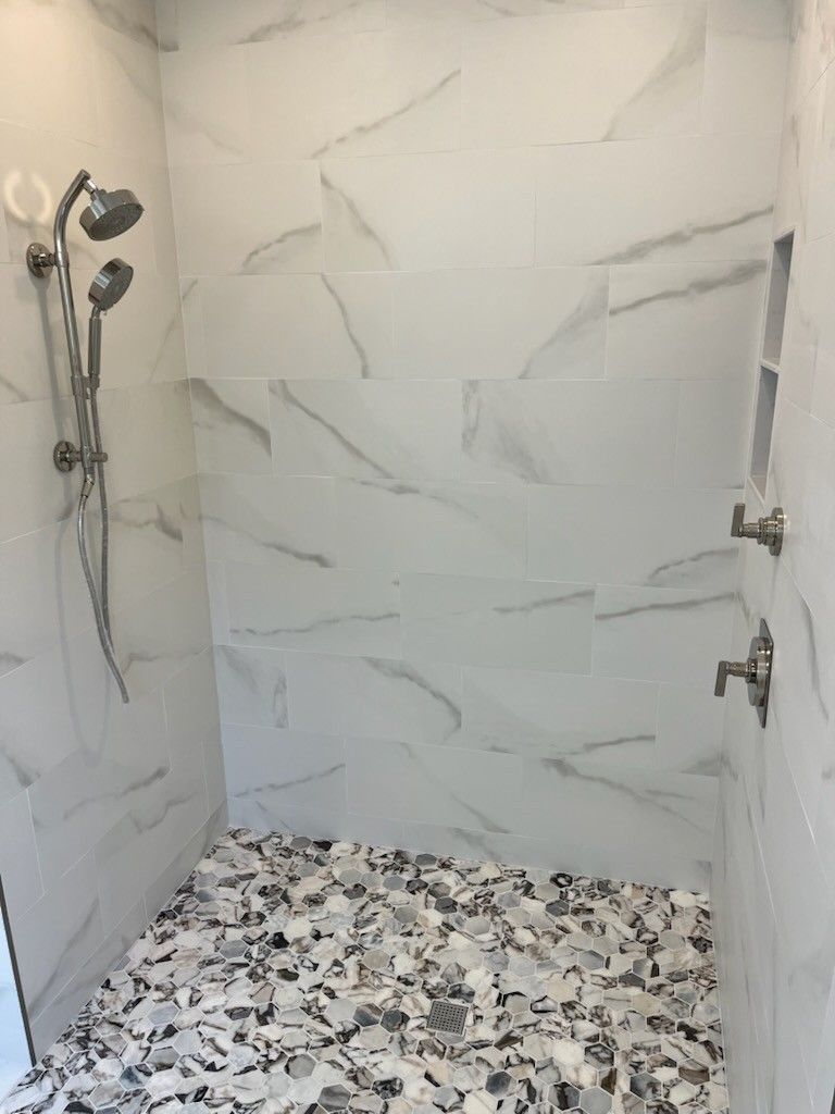 Shower with white marble-like tiles and mosaic floor. Silver shower head and fixtures.