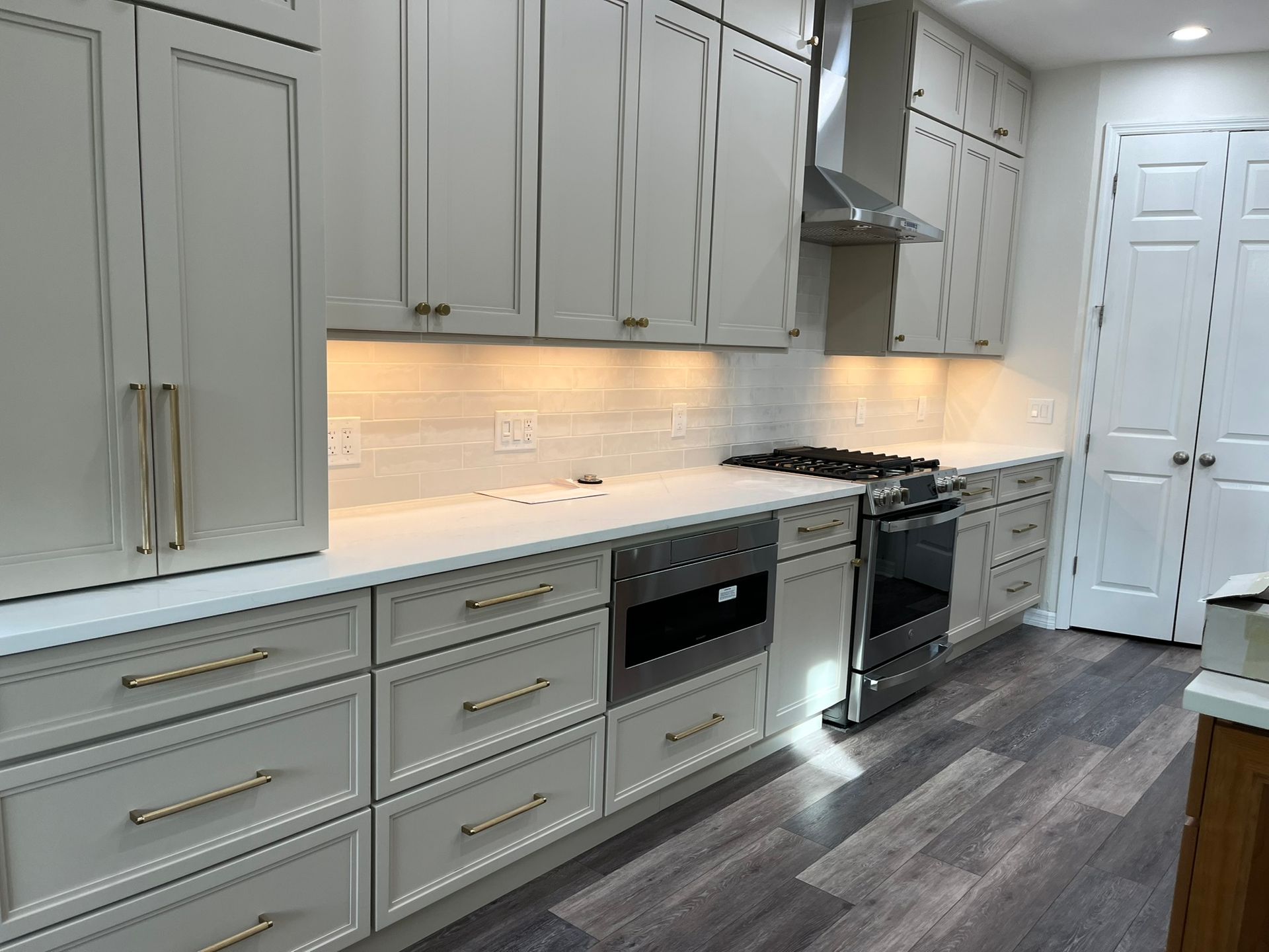 Light gray kitchen cabinets with gold hardware and white countertops.