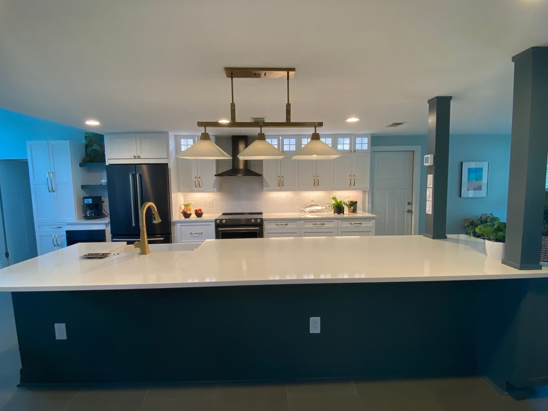 Modern kitchen with white countertops and teal island, black appliances, gold faucet, and pendant lighting.