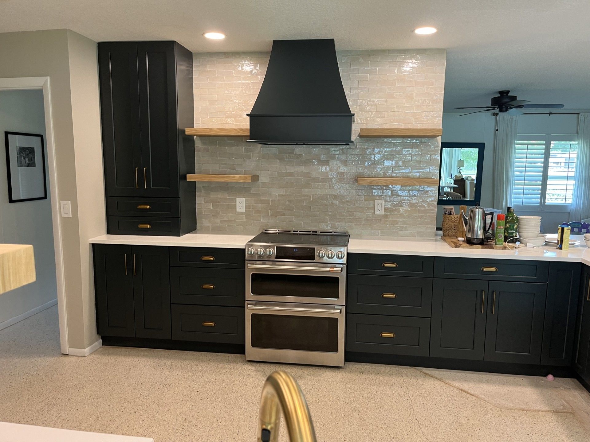 Black kitchen cabinets with a stainless steel range, light-colored backsplash, and floating shelves.