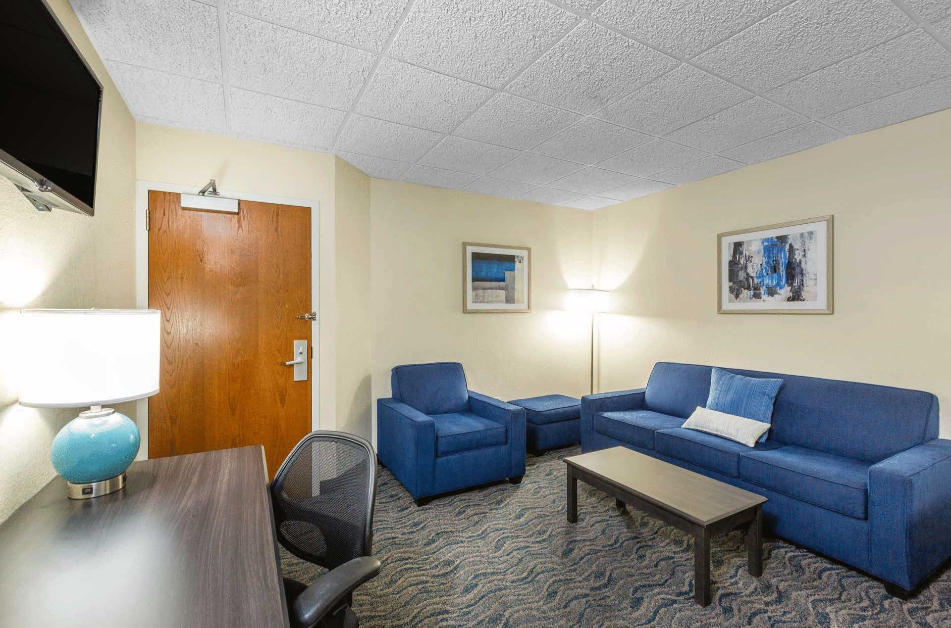 A hotel room with a couch , chairs , table and television.