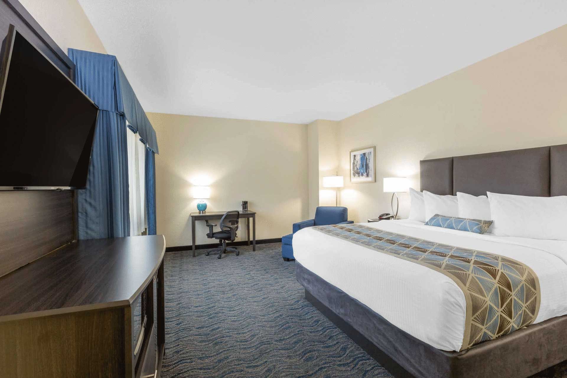 A hotel room with a king size bed , desk , chair and television.