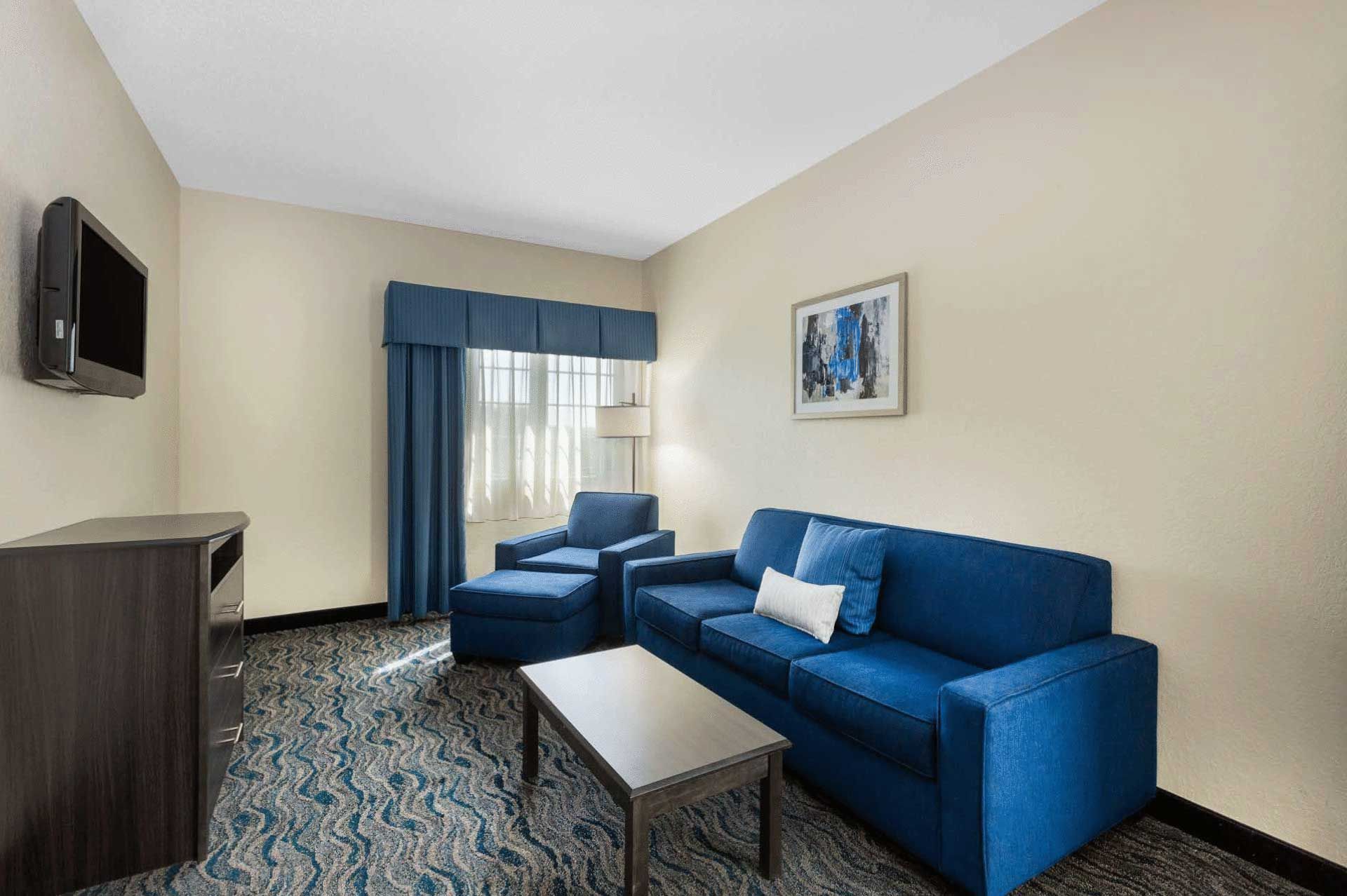 A hotel room with a blue couch , chair , table and television.