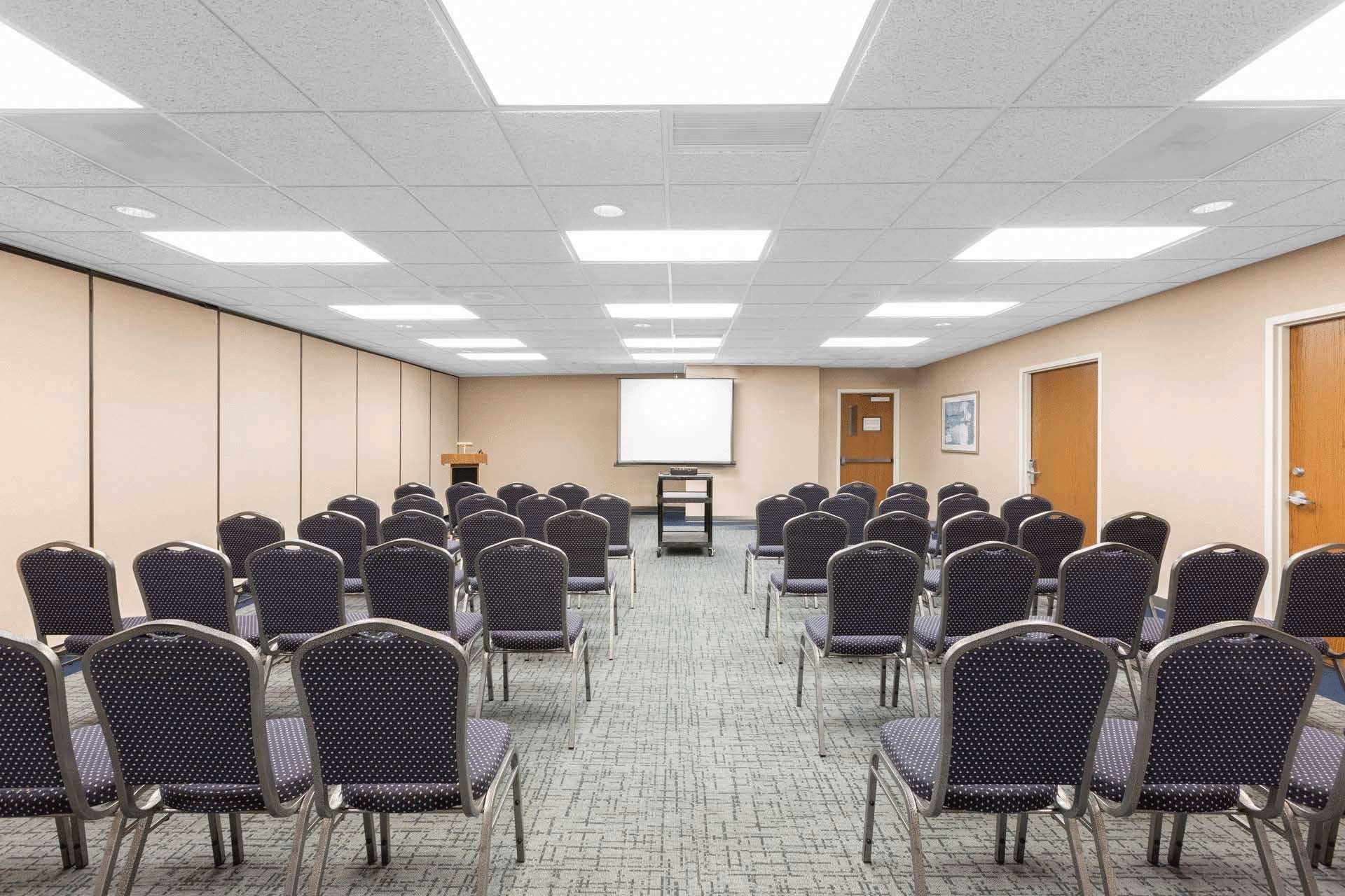 A large conference room with rows of chairs and a projector screen.