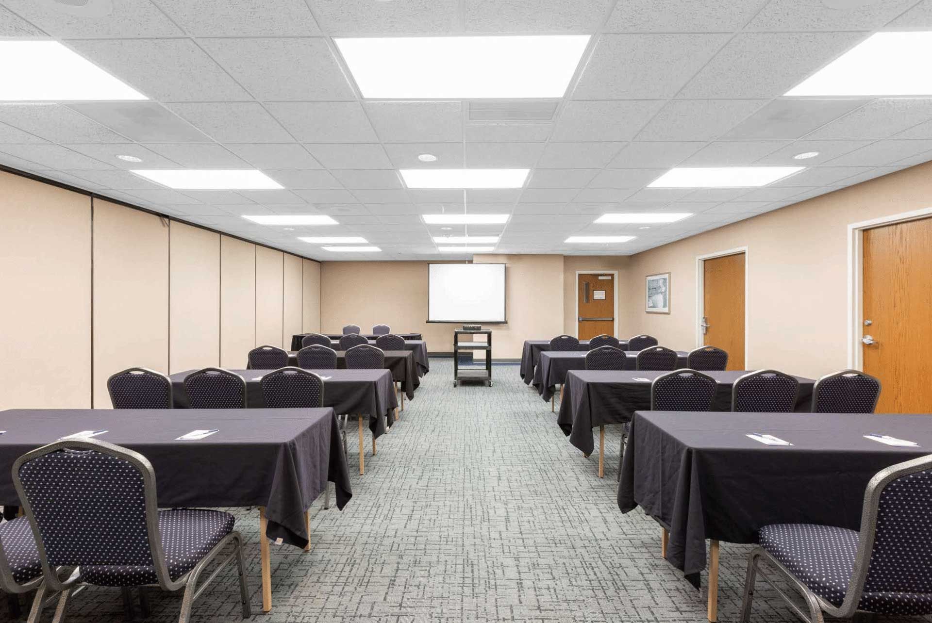 A conference room with tables and chairs and a projector screen.
