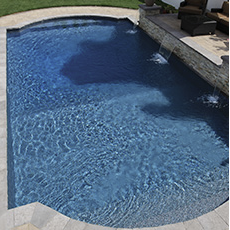 Blue swimming pool with a stone waterfall feature, next to a seating area.