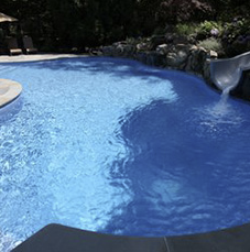 Blue swimming pool with a water slide and surrounding landscaping.