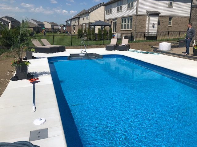 Backyard swimming pool with blue water beside a row of houses on a sunny day
