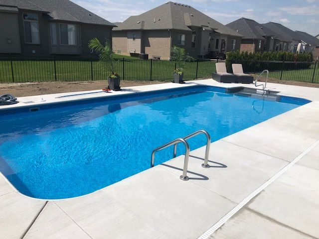 Backyard swimming pool with clear blue water, concrete deck, and suburban houses in the background