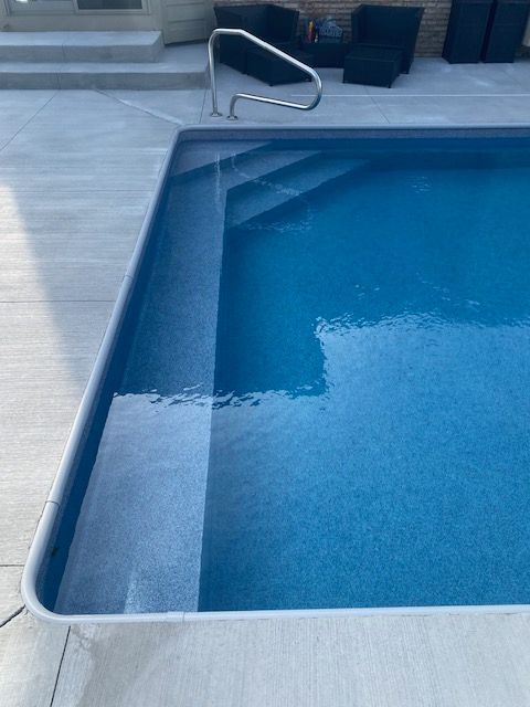 Outdoor swimming pool with clear blue water and stainless steel handrail by the steps