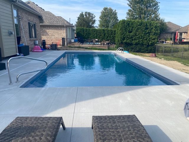 Backyard swimming pool with blue water, concrete deck, lounge chairs, and house patio.