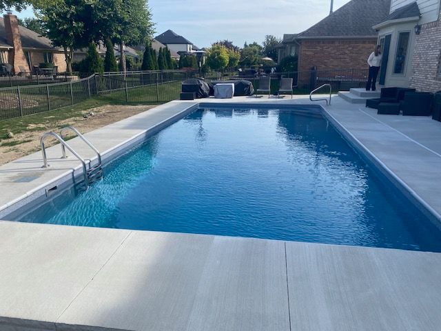 Backyard swimming pool with clear blue water and patio seating beside a house