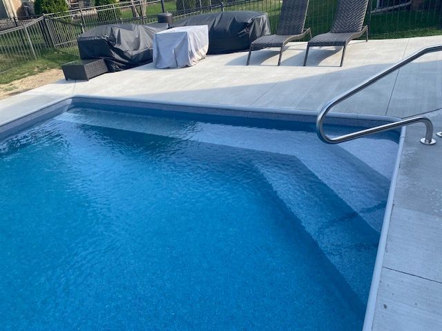 Backyard swimming pool with blue water, lounge chairs, and a patio table in the background
