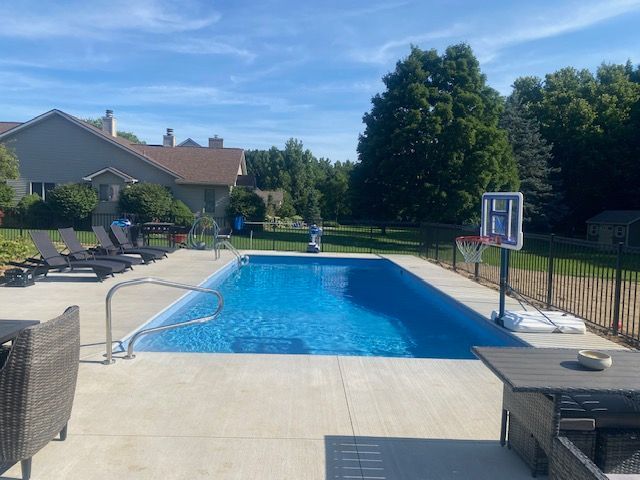 Backyard pool with lounge chairs, basketball hoop, and clear blue water on a sunny day