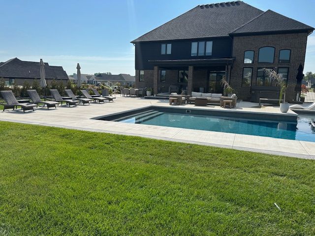 Modern house with a backyard pool, lounge chairs, and green lawn under a clear sky