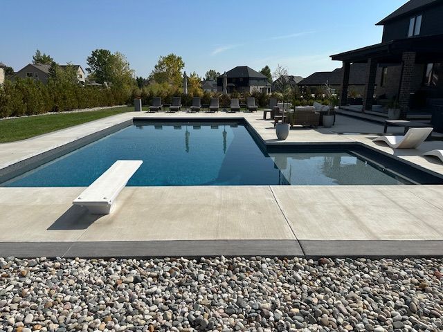 Backyard swimming pool with a diving board, hot tub, patio seating, and landscaped yard