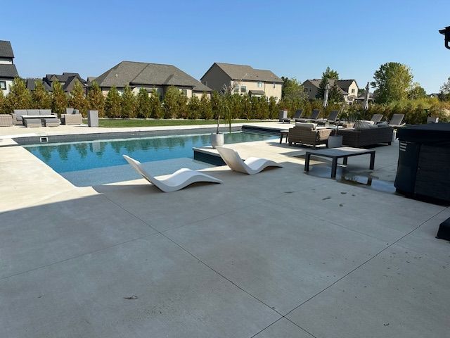 Modern poolside patio with lounge chairs, tables, and a swimming pool under a clear blue sky