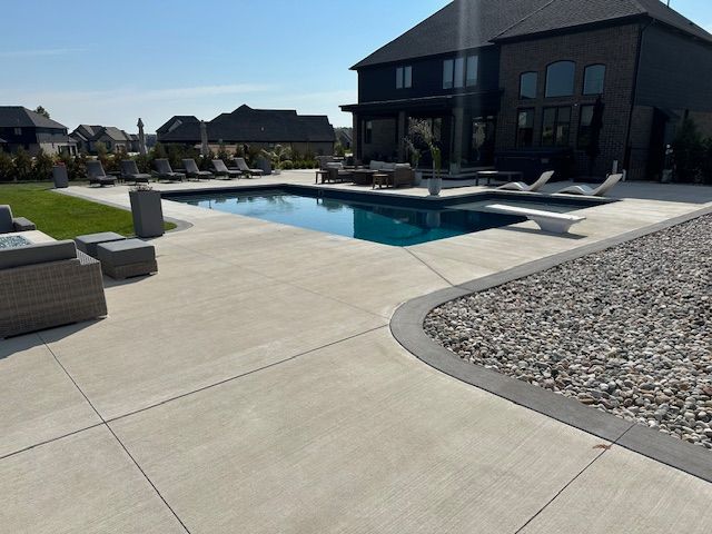 Modern backyard with a swimming pool, patio seating, and a dark two-story house under a clear sky