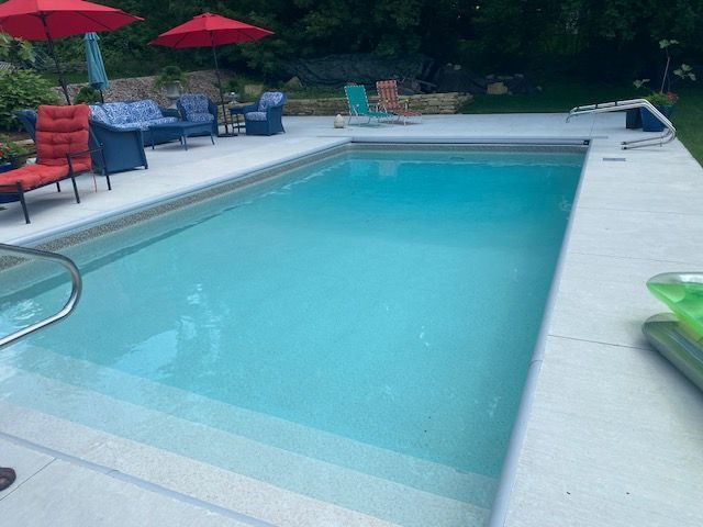 Outdoor swimming pool with blue water, white deck, red umbrellas, and lounge chairs surrounded by trees