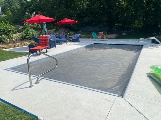 Empty outdoor pool deck with a covered pool, red umbrellas, and lounge chairs by trees