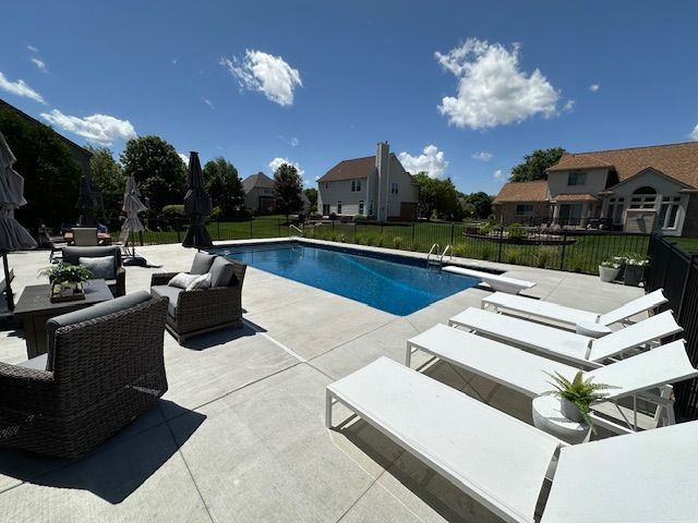 Backyard pool with lounge chairs and patio seating under a sunny blue sky