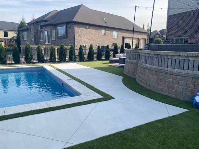 Backyard pool with concrete patio, green lawn, and brick house on a sunny day