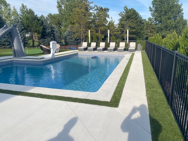 Backyard swimming pool with diving board, lounge chairs, and black fence on a sunny day