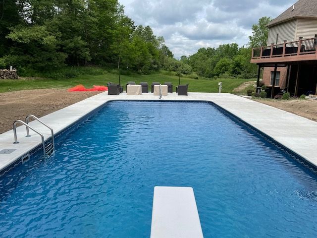 Backyard swimming pool with white deck, ladder, lounge chairs, and covered patio under cloudy sky
