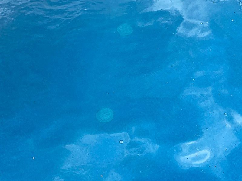 Azure water with visible cloud reflections, and a few round objects beneath the surface.