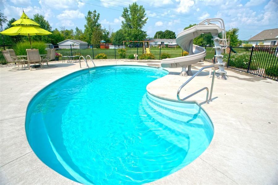 Swimming pool with a water slide, stairs, and patio furniture on a sunny day.