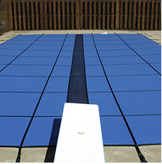 Blue pool cover stretched over a swimming pool, a diving board in the foreground.