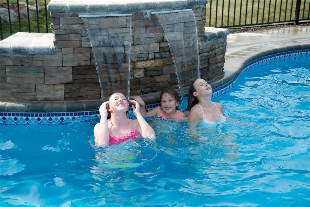 Three people enjoying water cascading from a stone feature in a pool.