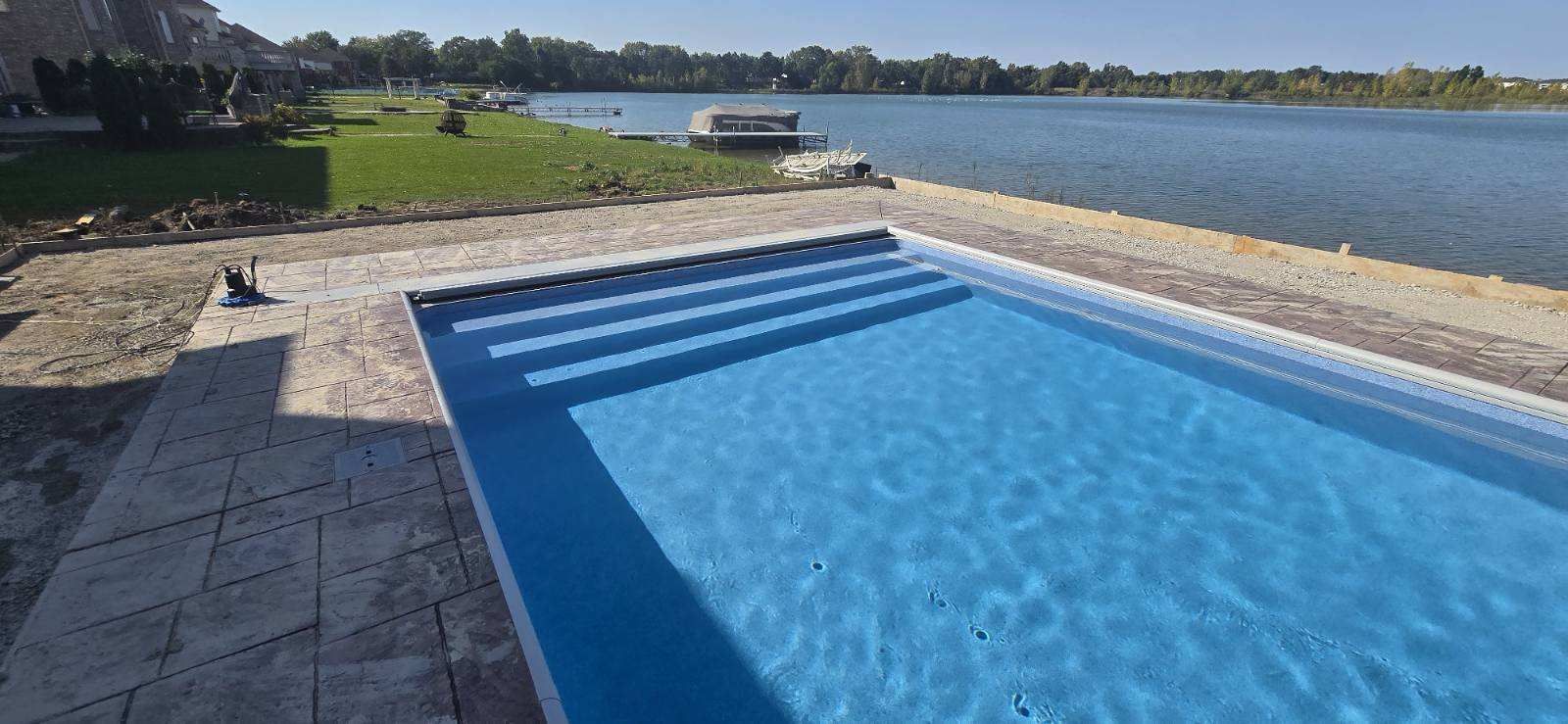 Blue swimming pool beside a grassy lakeside with a docked boat in the distance
