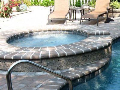 Hot tub next to a pool with brick edging. Loungers and table in background.