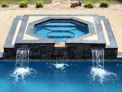 Swimming pool with a raised spa, stone waterfall features, and blue water.