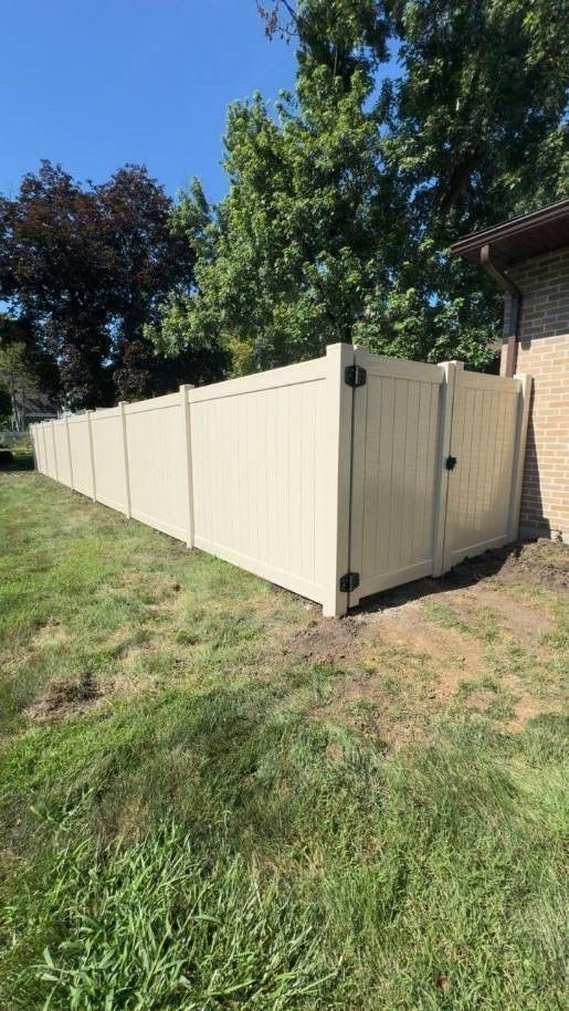 Beige vinyl fence enclosing a backyard beside a house and trees under a blue sky