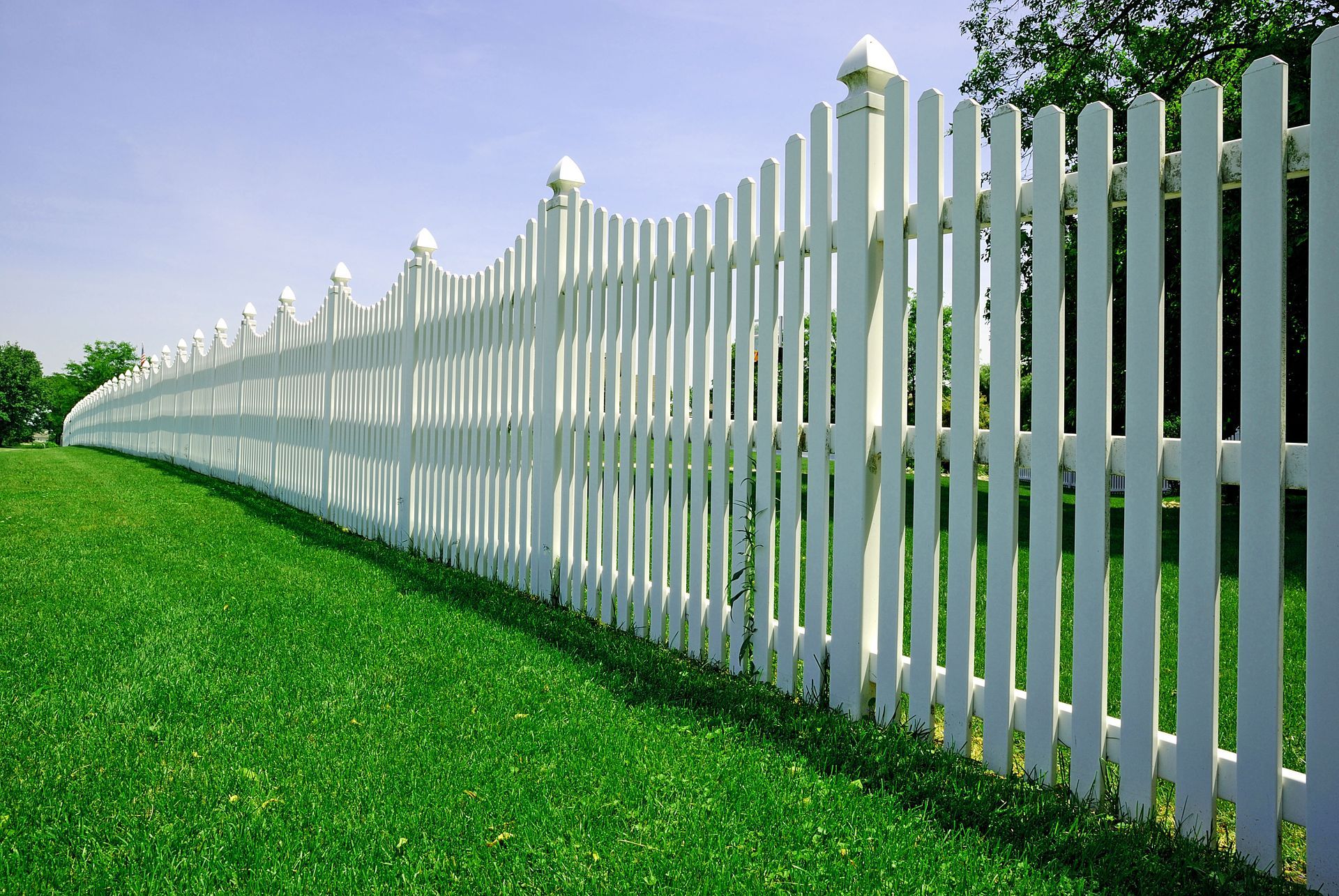 White picket fence in a green field with a blue sky in the background.