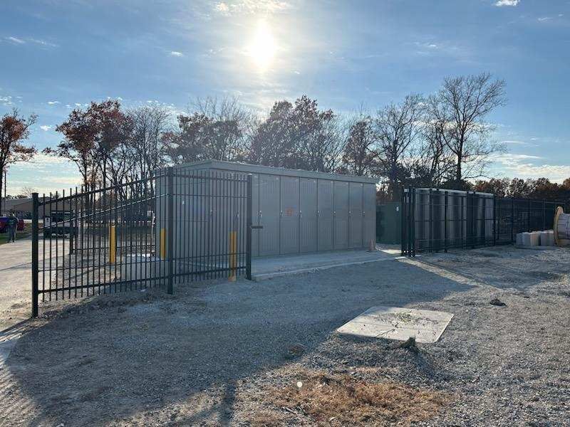 Storage units behind a black metal fence, under a sunny sky.