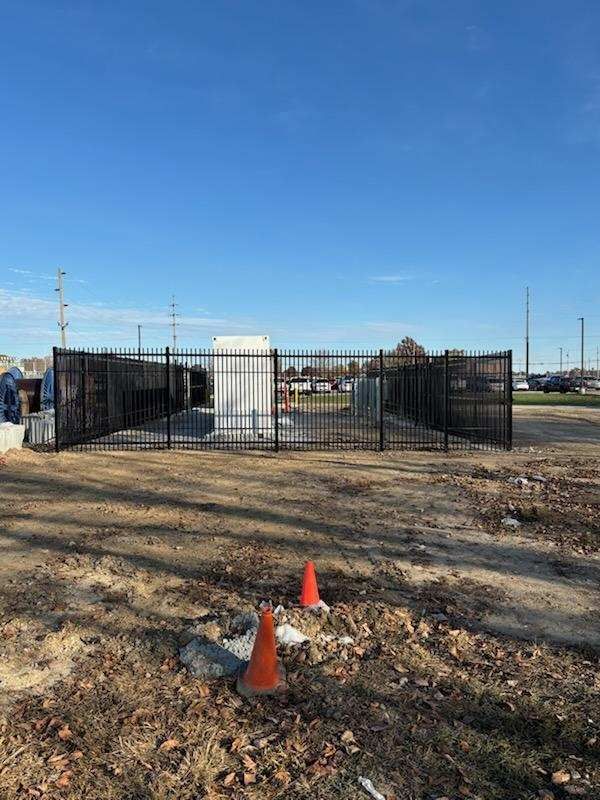 Fenced enclosure on a dirt lot; two orange traffic cones in foreground; clear blue sky.