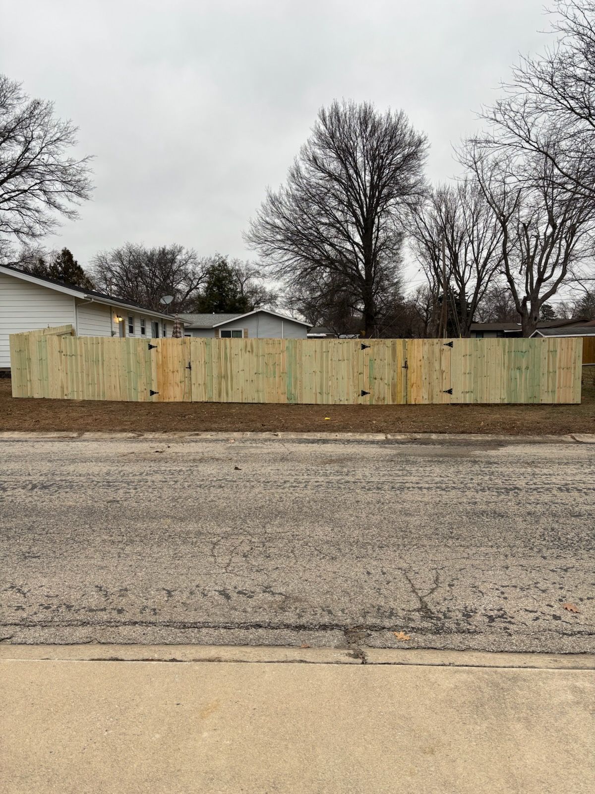 Wooden fence bordering a yard, viewed from the street on an overcast day.