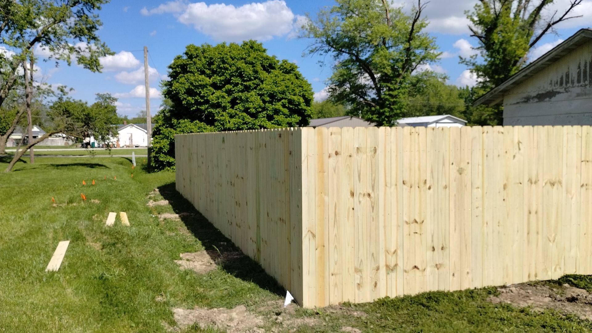 A newly installed light-colored wooden fence standing in a grassy yard on a sunny day.
