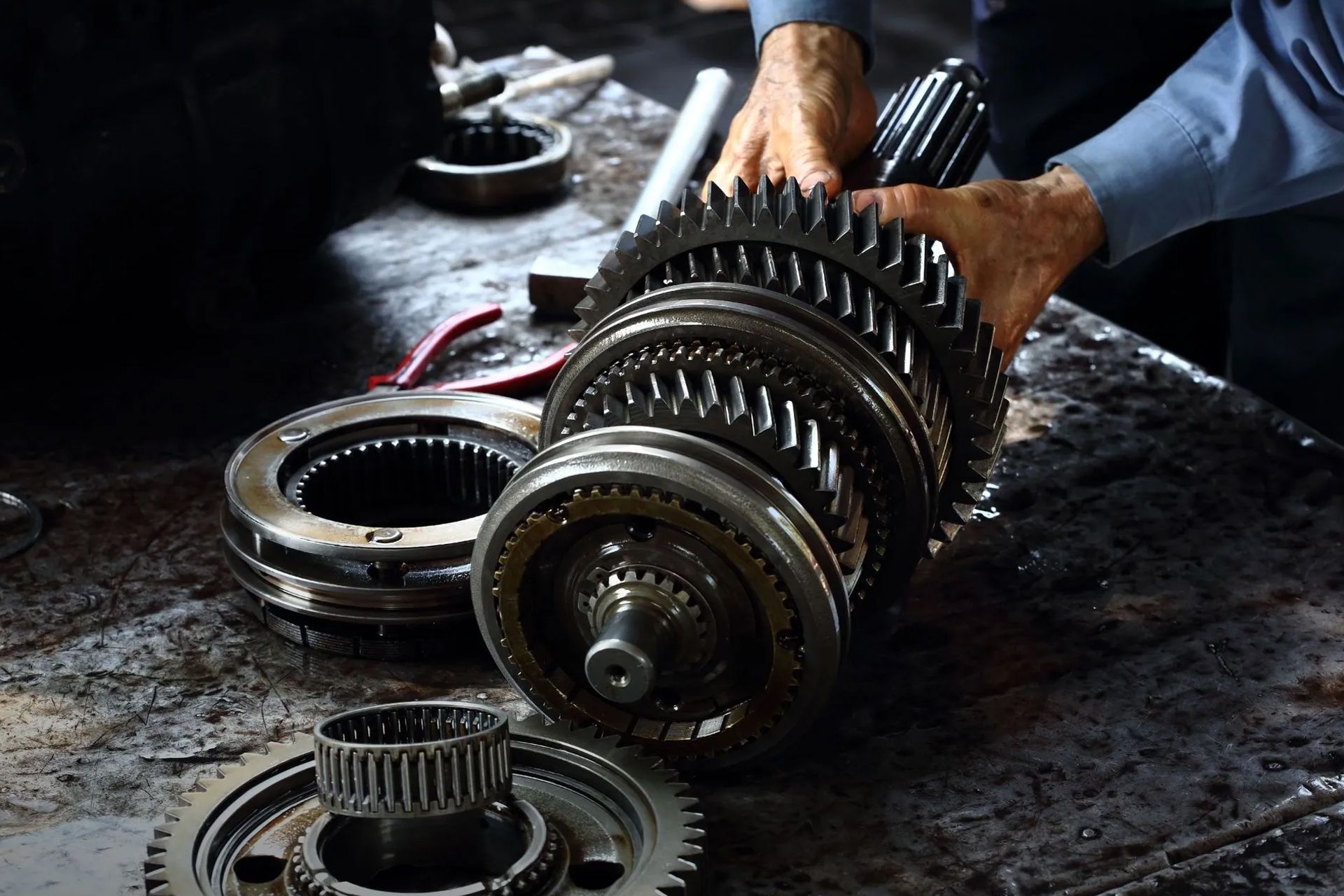 Hands holding gears, part of a car transmission, on a workbench.