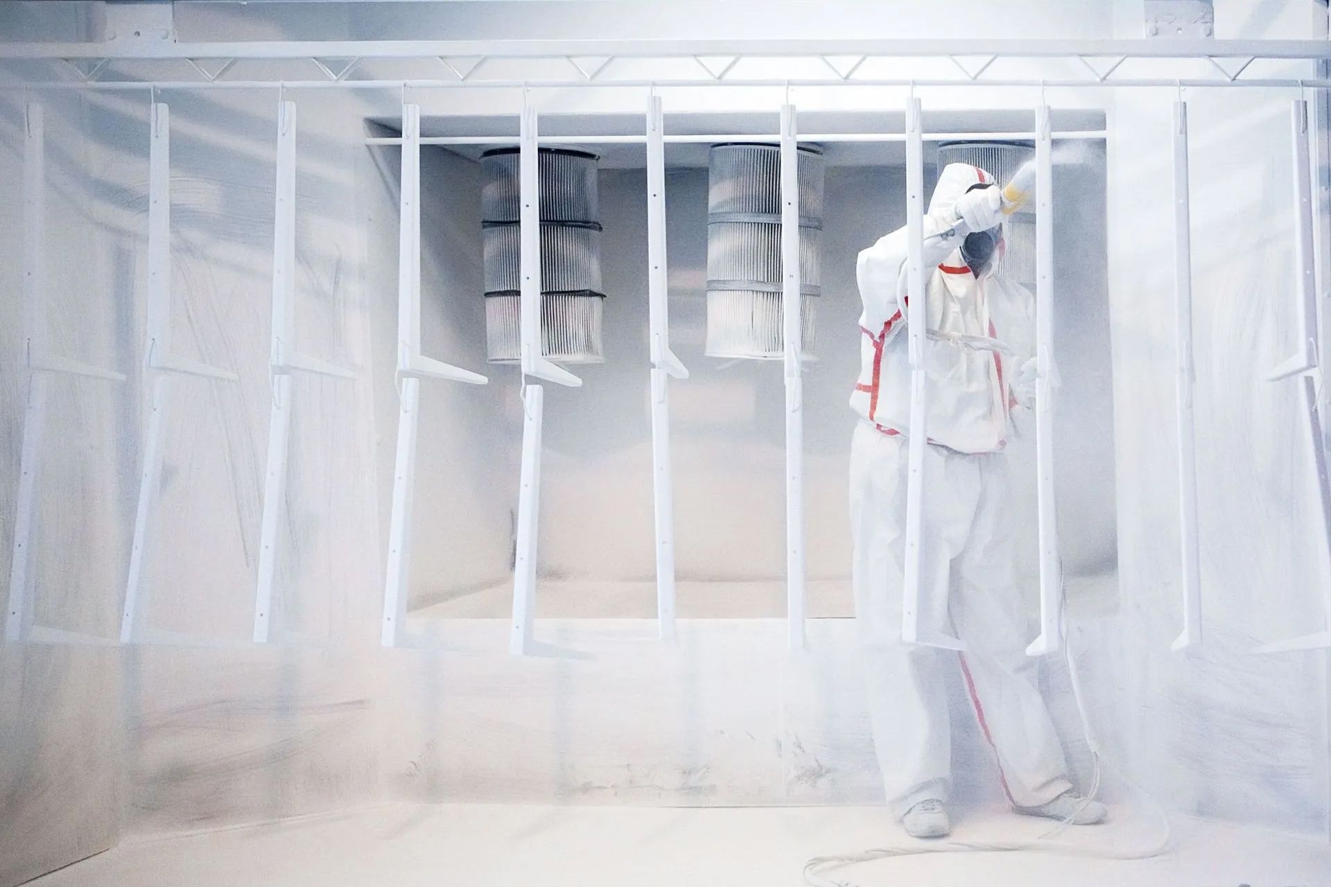 A person in a white protective suit painting in a white spray booth.